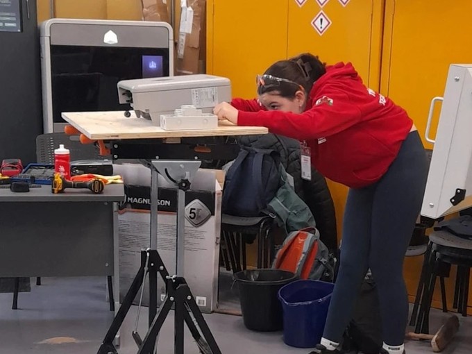 Emily in a red branded skills hoodie bending looking at equipment during a skills competition