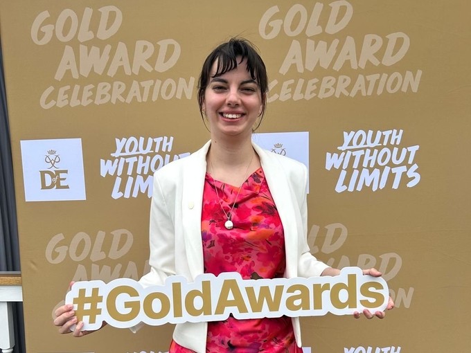 Lowri holding a gold awards sign in front of DoE branding