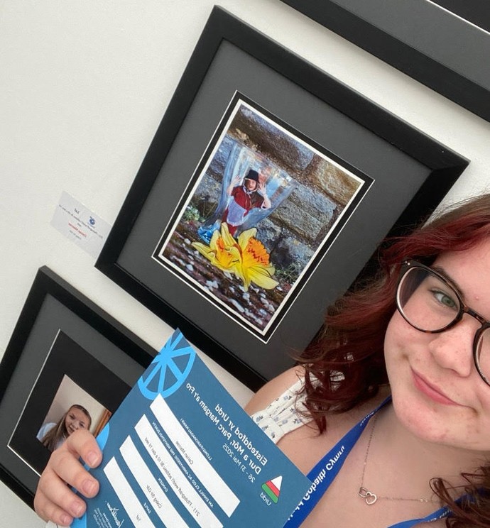 Ceirian - a selfie with her holding her score and with her imagery behind her (including traditional Welsh costume)