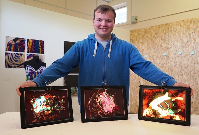 Philip holding three pieces of his work which are illuminated from the back