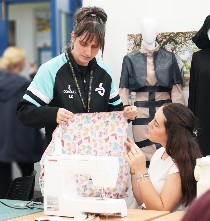 Lowri, A-level lecturer helping a student with fabric by a sewing machine