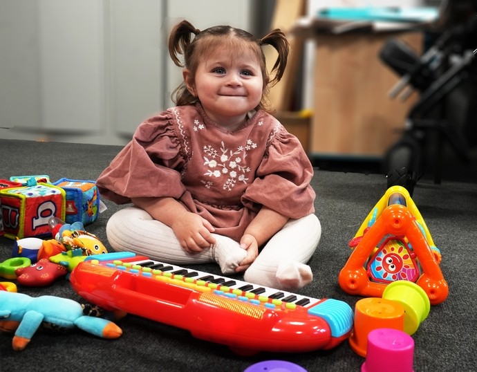 Liwsi playing with some toys smiling sitting on the floor