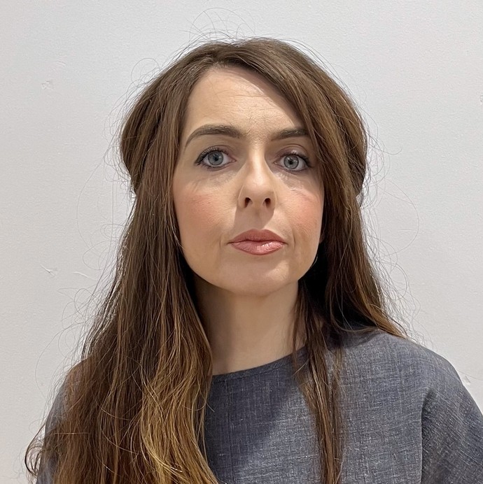 Nia facing the camera in a headshot in a grey uniform