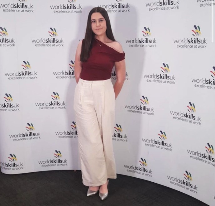 Emily with WorldSkills branding behind her she is dressed smartly
