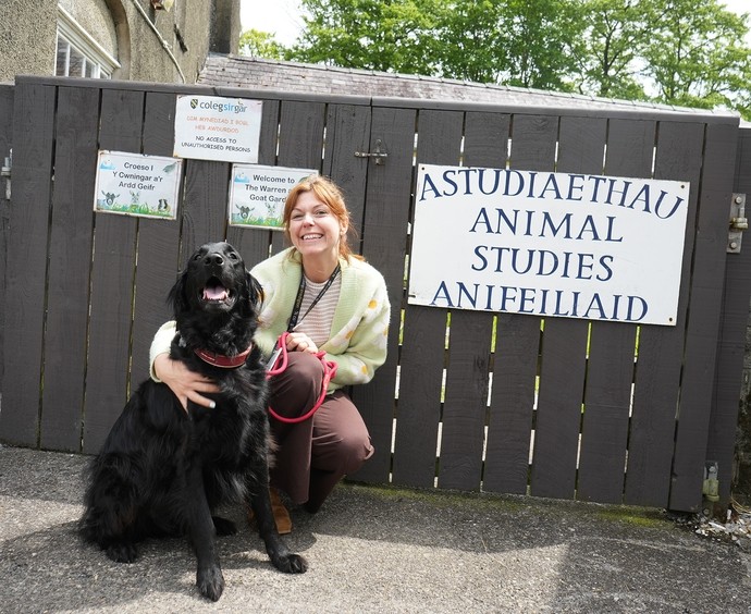 Lecturer Hayley kneeling outside with a dog with the sign saying animal and equine centre