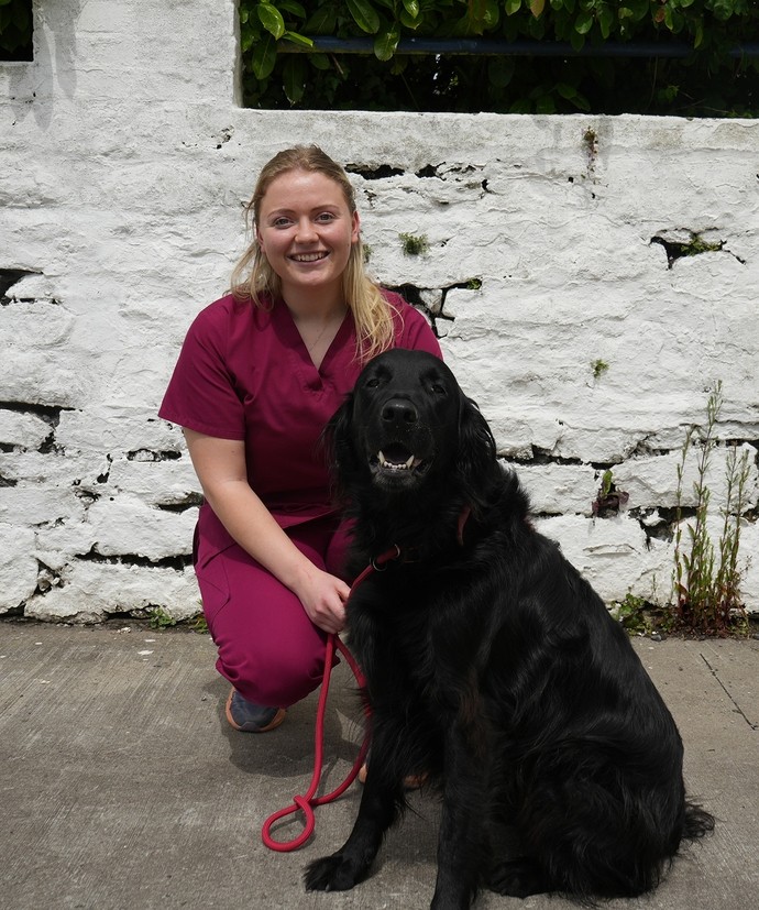 Sarah in her vet scrubs kneeling outside with a dog