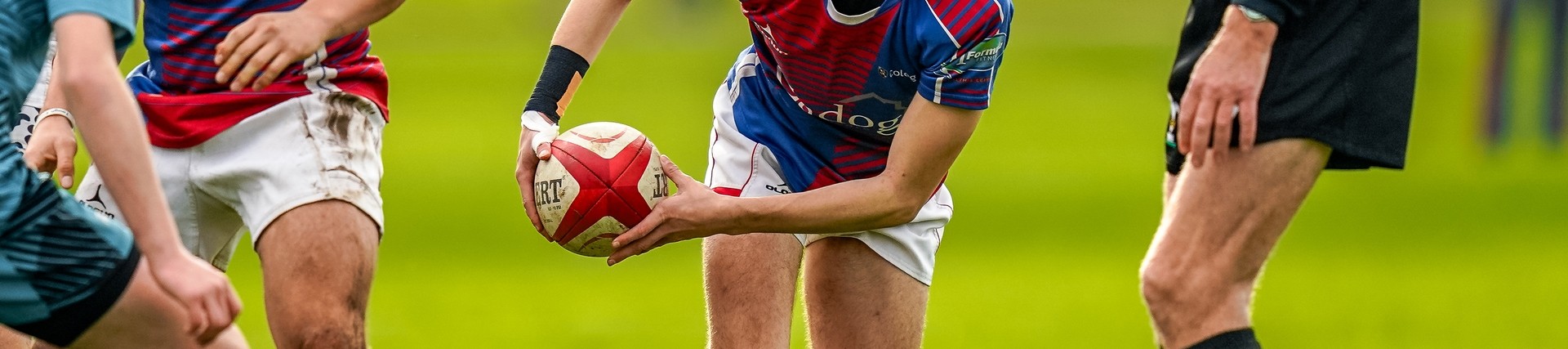 Action shot of student in red and blue sports kit playing rugby.