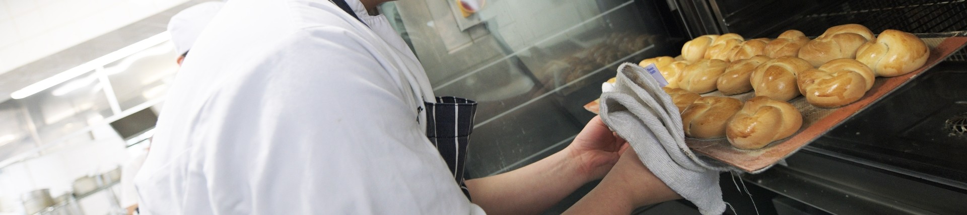 A person in chef whites putting a try of food into a large oven.