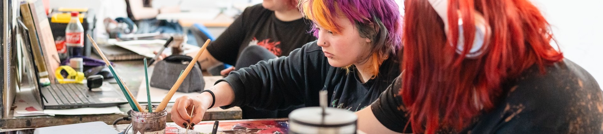Three students working on artwork at desk