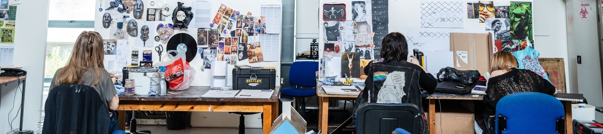 Three students working at desks doing artwork 