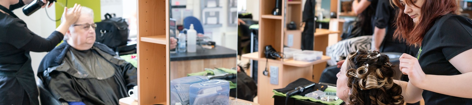 two students in hairdressing classroom with clients