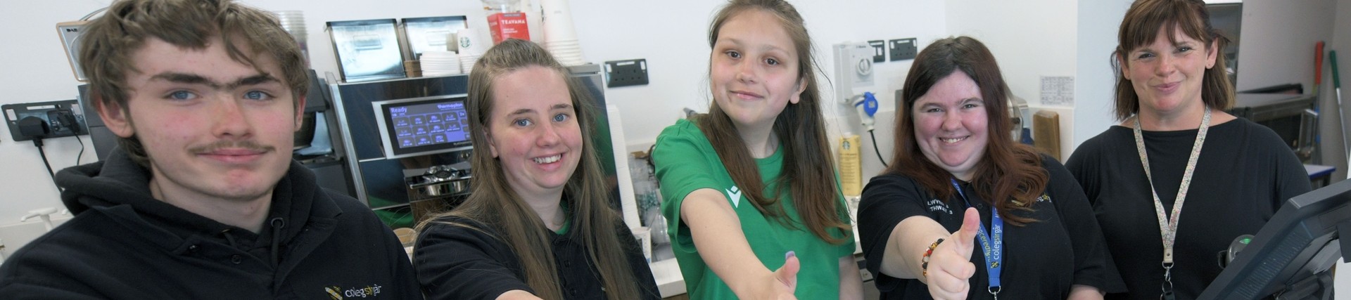 Group of internship students standing behind a cafe counter with their thumbs up