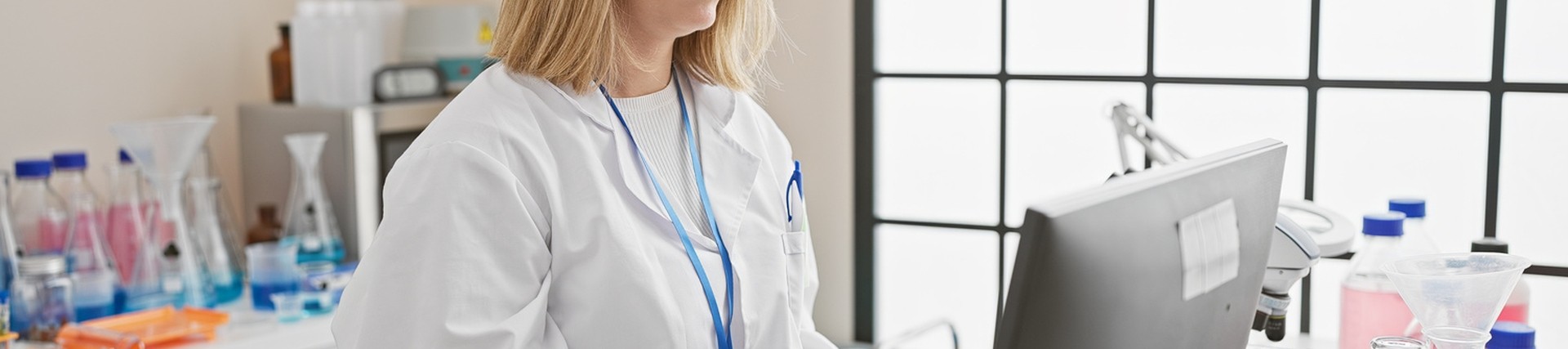 Blonde woman working in a hospital, typing on a computer wearing office scrubs