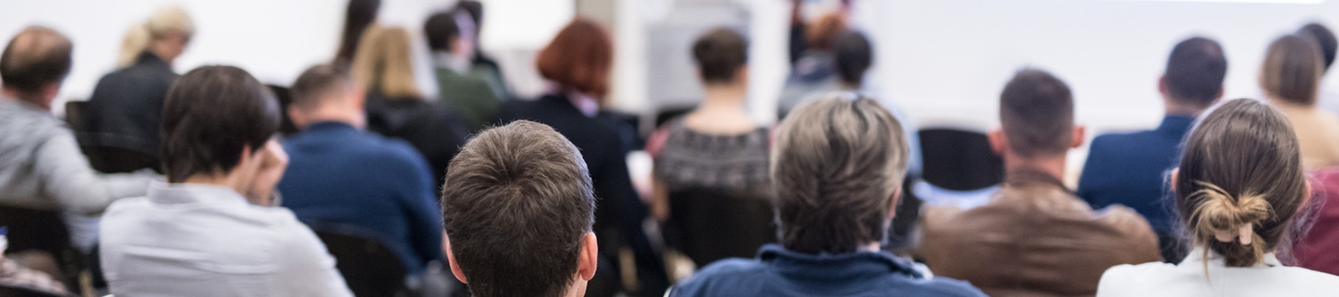 Ystafell o bobl yn eistedd gan wynebu ymlaen tuag at siaradwr yn ystod seminar