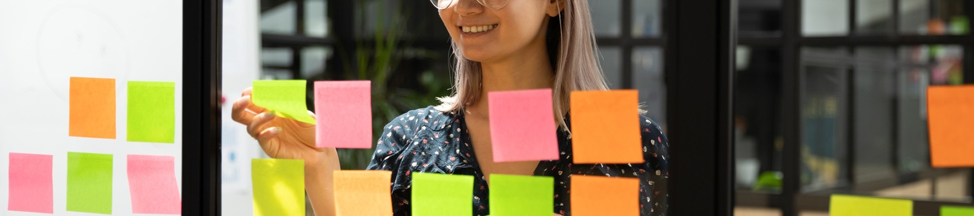 Woman wearing glasses sticking sticky notes not a glass window, the shot taken from the other side of the glass, looking directly at the person