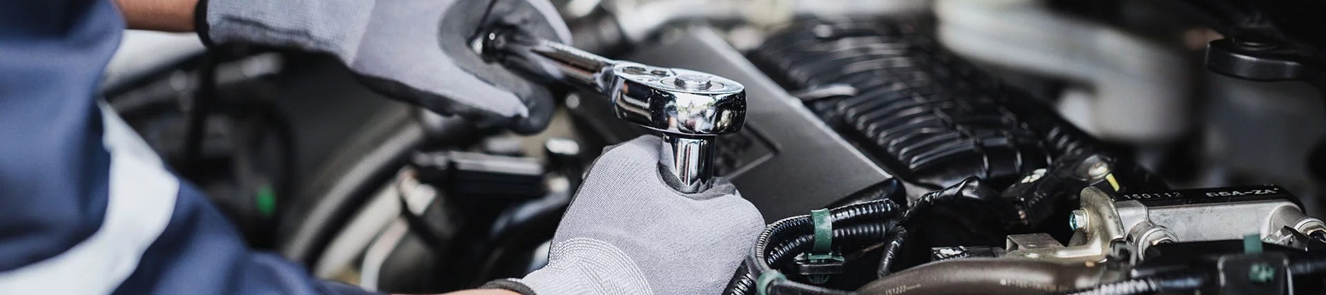 Hands of an unseen person working a car engine using a wrench