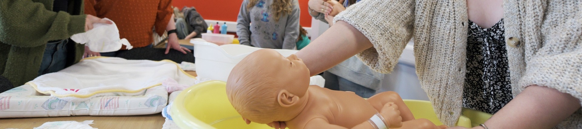 A group of childcare students practicing bathing a baby doll in a yellow bathtub