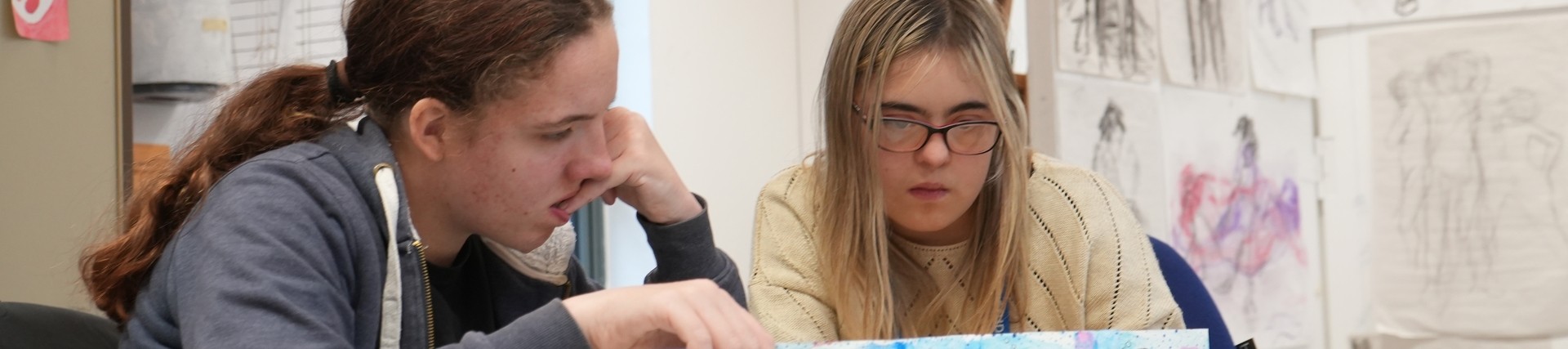 Two students engrossed in their artwork at a desk