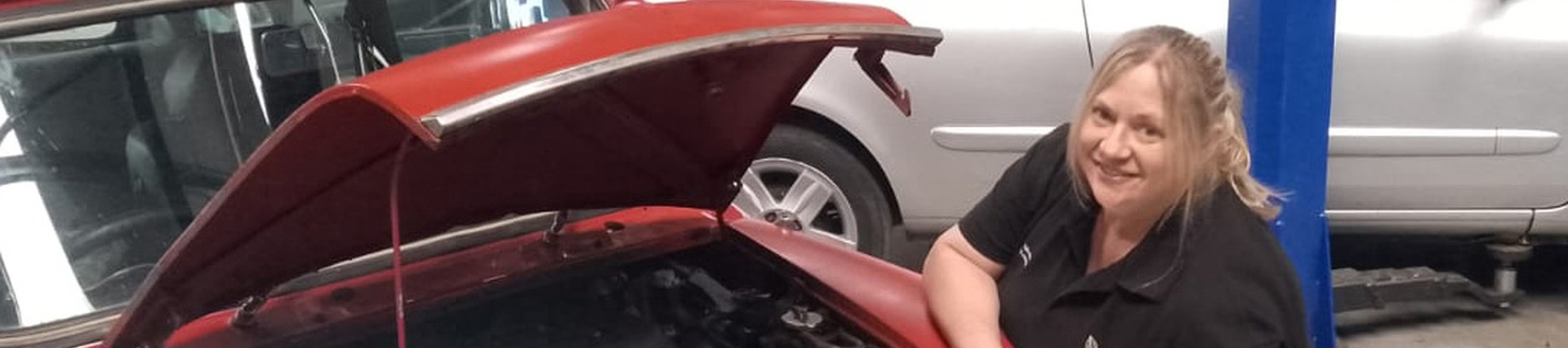 Trudy bending down with a bonnet of a mini up showing the engine