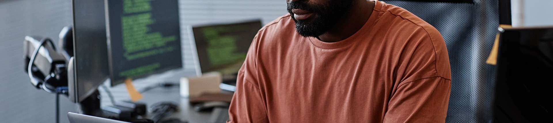 Black male wearing glasses and an orange t shirt working on a laptop