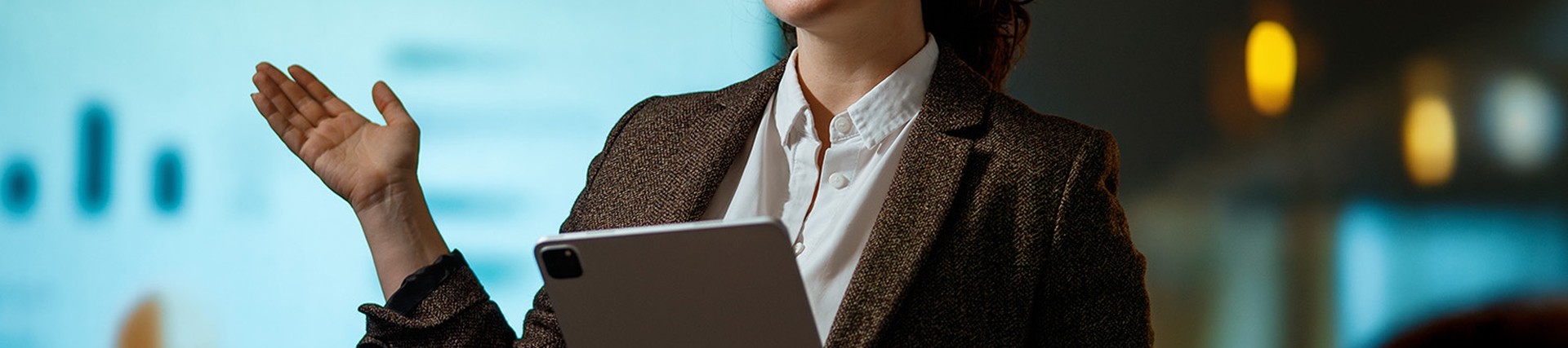 Brunette female wearing glasses and brown blazer giving a presentation in front of a screen