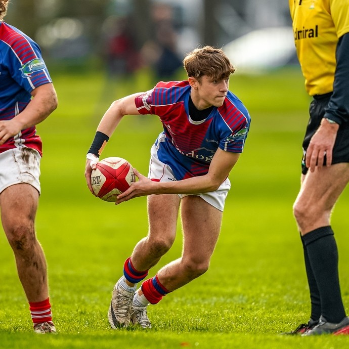 Action shot of student in red and blue sports kit playing rugby.