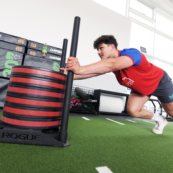 Student in sports kit pushing a sled in the gym.