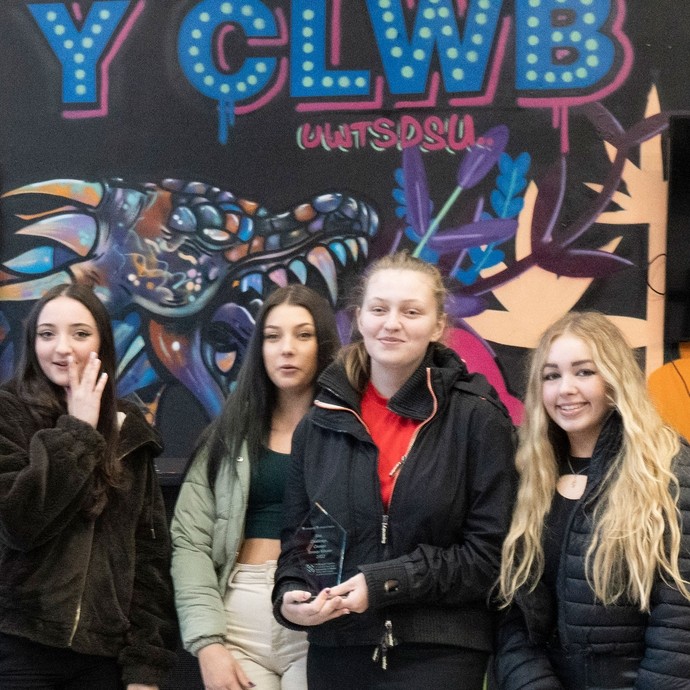 Students standing under a sign saying Y Clwb