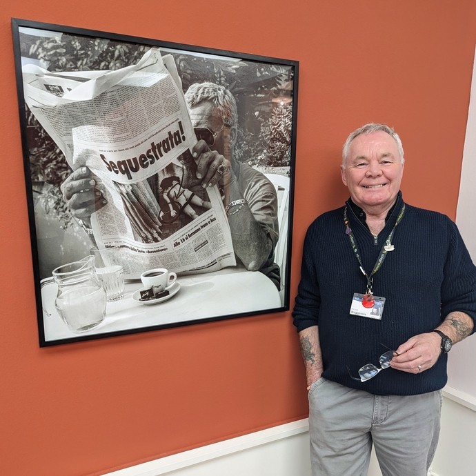 A tutor standing next to a photo of a man reading a newspaper