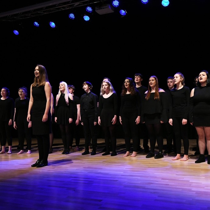 Choir in black singing in a well lit theatre