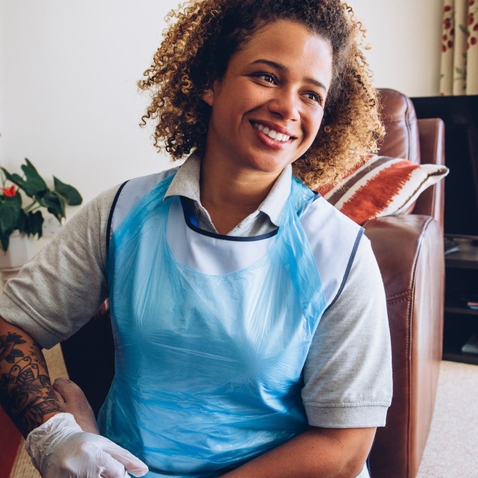 A carer, wearing a blue medical apron, puts a bandage on a patient's ankle