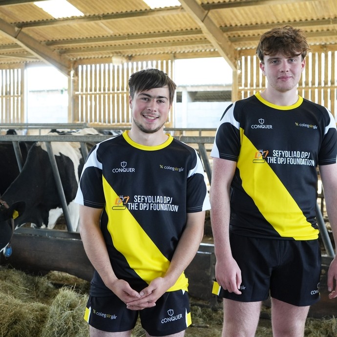 two boys in a cow shed wearing the black and yellow kit