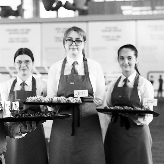black and white image of hospitality students in uniform holding a plate of canapes