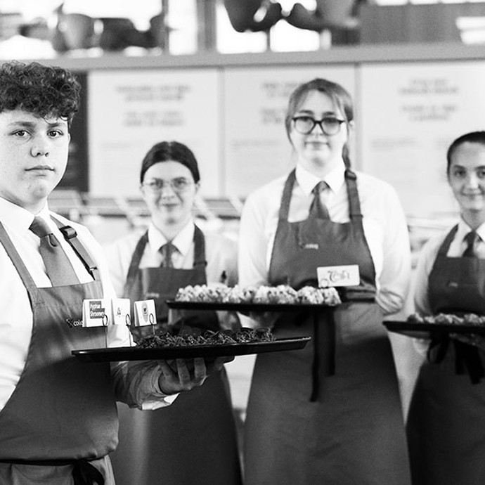black and white image of hospitality students in uniform holding a plate of canapes