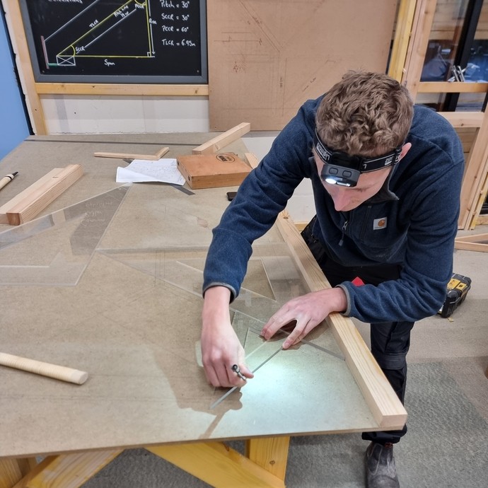 A person working on a workbench with a technical drawing in the background