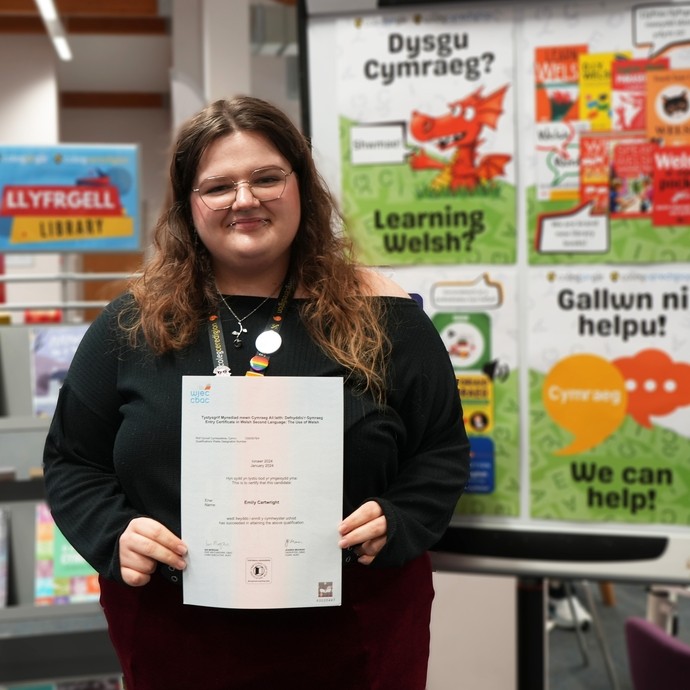 Emily with the library in the background holding her certificate