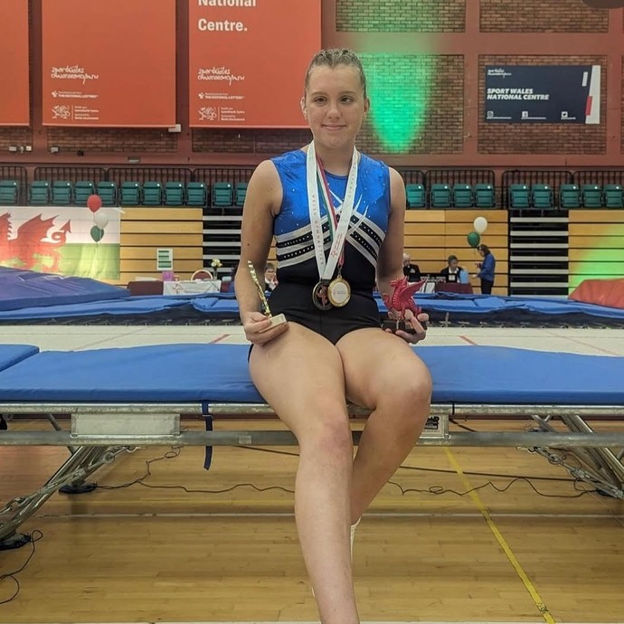 Maddie in professional gym kit with a medal leaning on a trampoline
