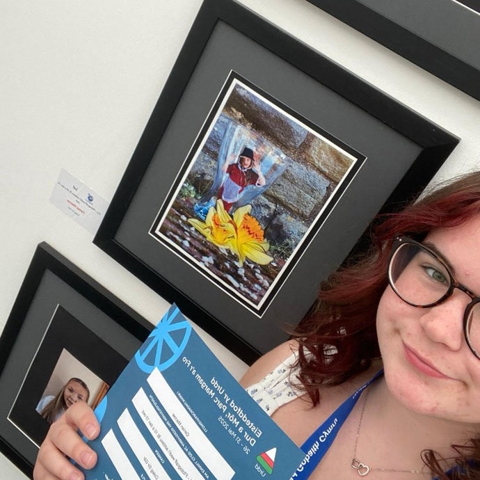 Ceirian - a selfie with her holding her score and with her imagery behind her (including traditional Welsh costume)