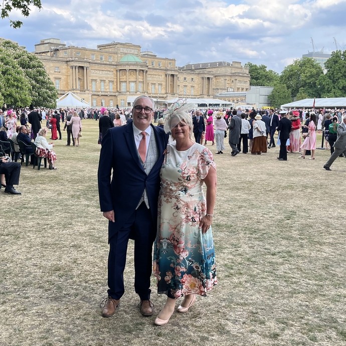 Rob and his wife Michele standing together in grassy grounds behind Buckingham Palace