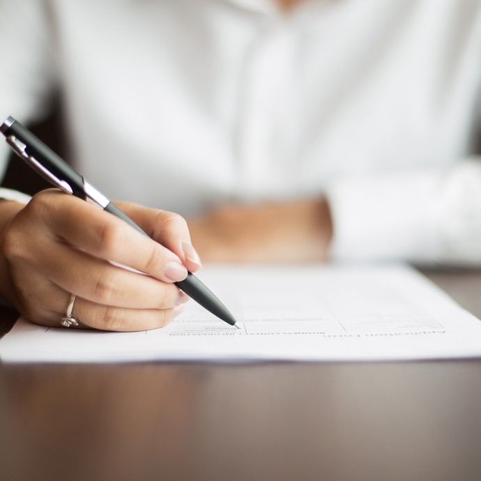 close up shot of someone in a white shirt signing a document