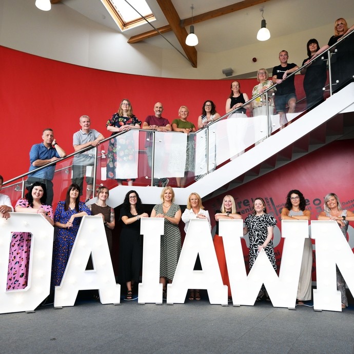 All the A-level tutors lined up on the stairs and balcony with the lighted up words Da Iawn at the bottom 