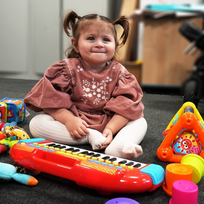 Liwsi playing with some toys smiling sitting on the floor