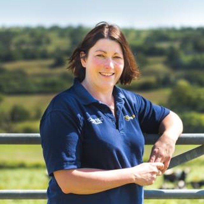 Liz standing and leaning on a fence outside with grassland behind her looking at the camera