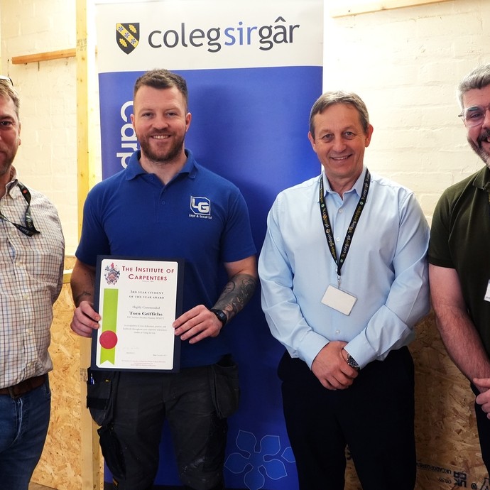 Tom standing with his certificate with tutor Gareth, Wayne and Craig in a carpentry workshop