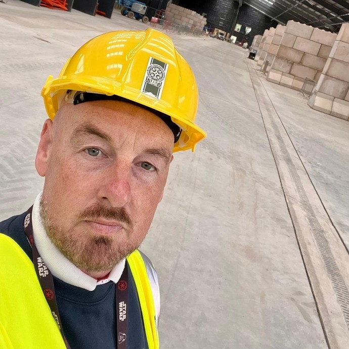 Richard a HR apprentice in a yellow construction hat with a warehouse type background