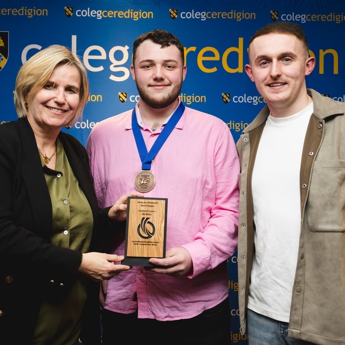 Acting principal Vanessa with Glyn and tutor Sam college branding behind Glyn holding skills competition Wales medal