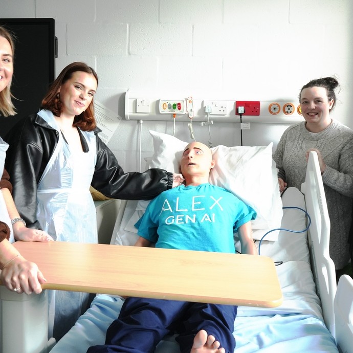 Alex the AI mannequin in a bed with a student and lecturer one side and the other Rebecca and Vicky