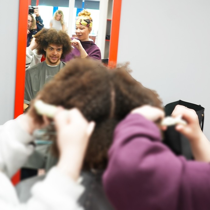 Two hairdressing students working with afro hair on a client who  you can see in a salon mirror